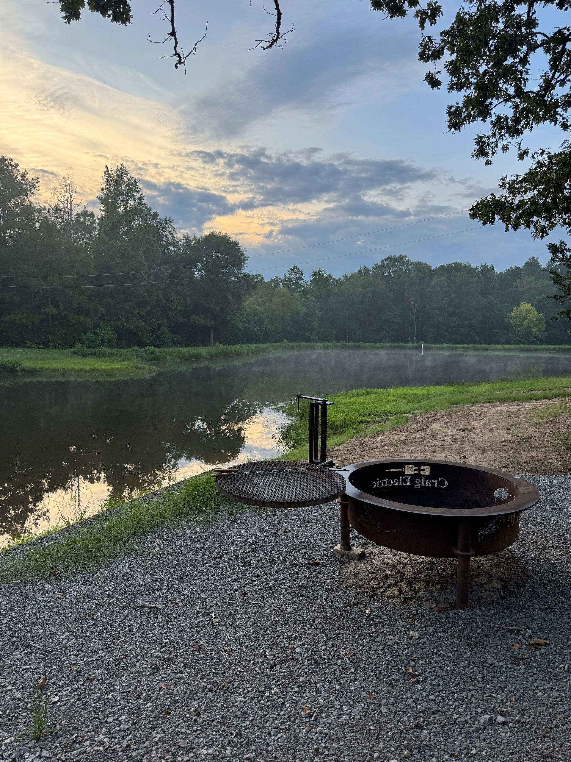 Custom fire pit and swing grill at dawn with mist over the pond